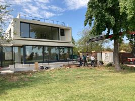 Casa blanca de dos pisos con fachada de vidrio hacia un jardín de pasto