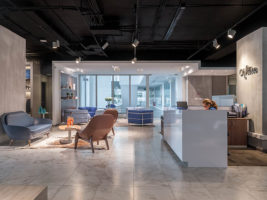 Recepción de oficina con piso de piedra clara, sillones tapizados y mesón blanco