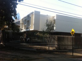 Edificio blanco de varios pisos detrás de una reja, rodeado de árboles
