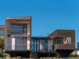 Casa de hormigón y revestimiento de madera, con terrazas y grandes ventanales bajo un cielo despejado
